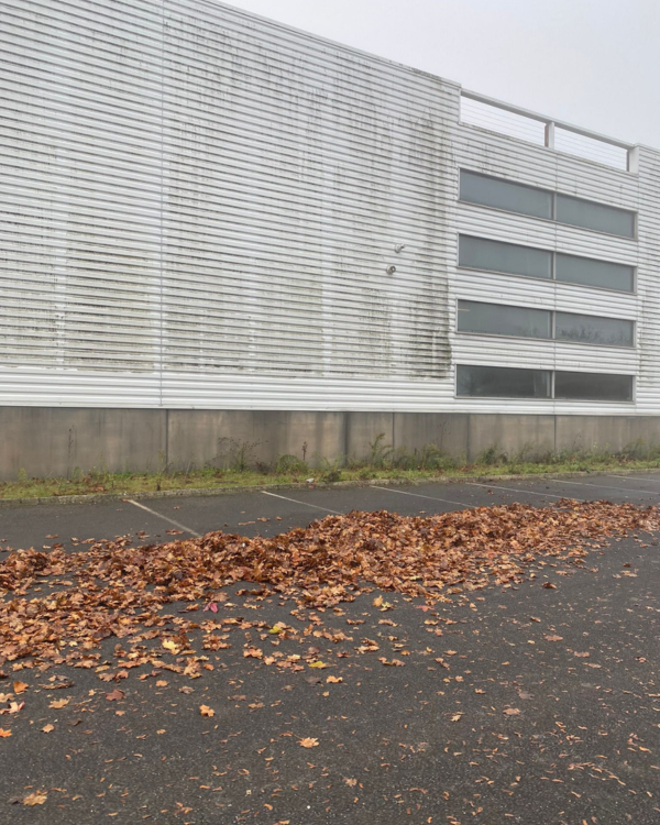 Façade de bâtiment industriel fortement encrassée pendant une intervention de nettoyage de bardage.