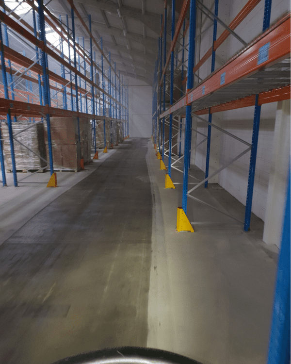 Nettoyage des allées de circulation au sein d'un entrepôt de stockage équipé de racks industriels.