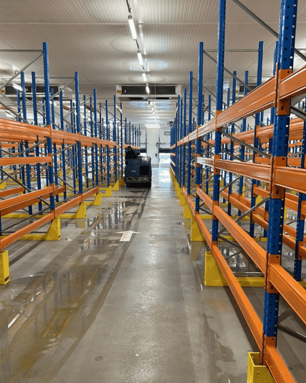 Nettoyage d'un entrepôt frigorifique avec une autolaveuse industrielle entre les racks de stockage.